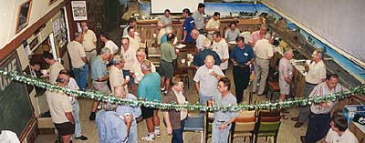 Colour picture: a meeting at AMRA's Rockdale clubrooms. The kitchen is at left; the N-scale layout is at the back; to the right is the Read area of the HO layout. The tinsel is suspended to show the extent of the demolition caused by the widening of Chapel Lane.